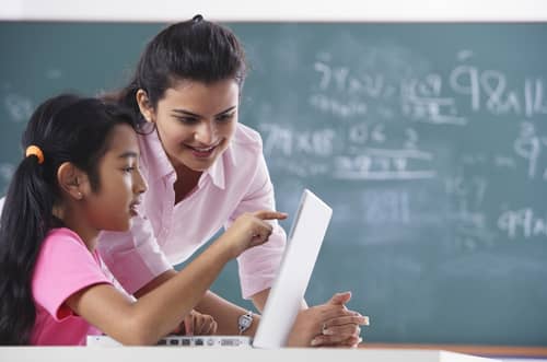 A female instructor and a student pointing to the screen on a laptop